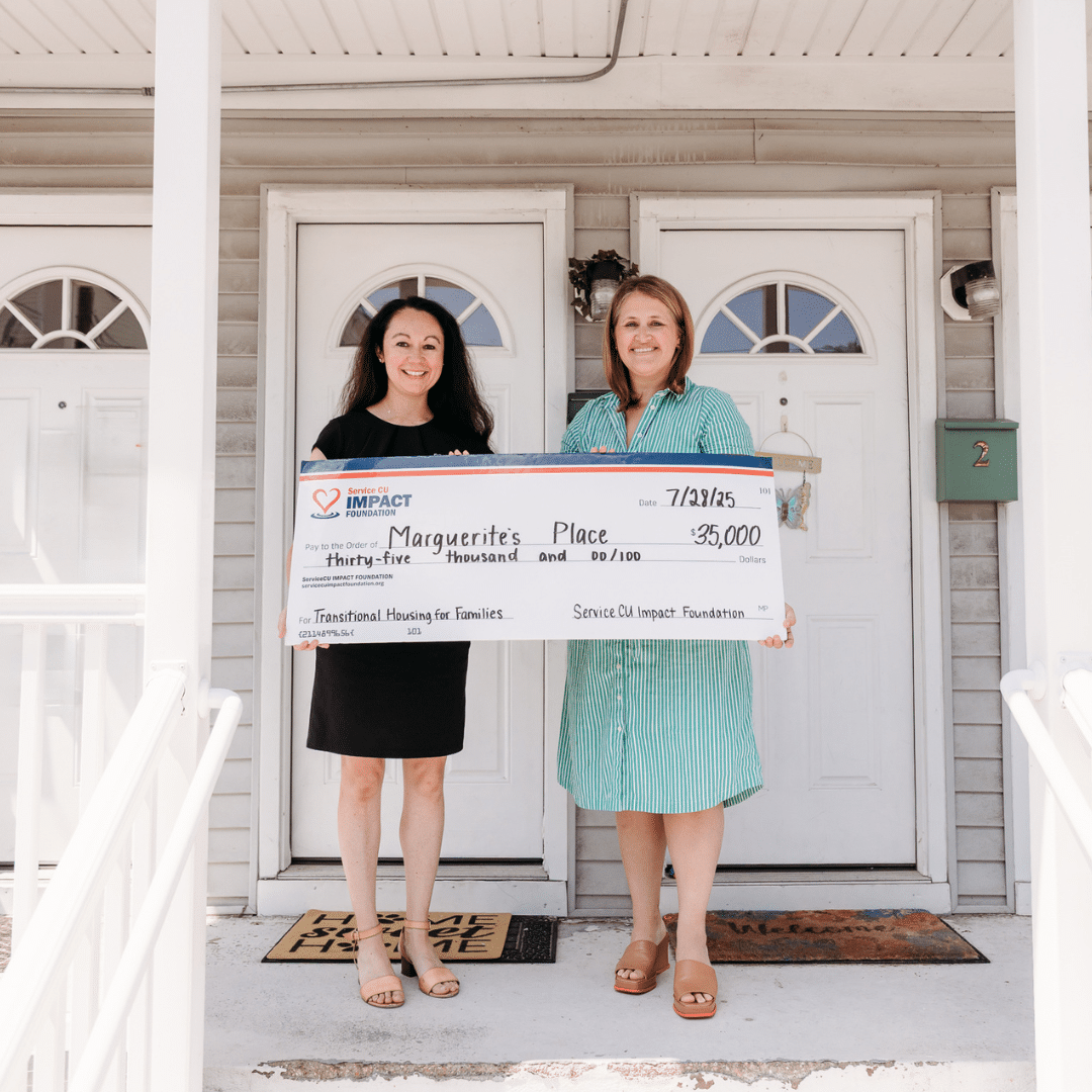 two women hold up a check from federal service credit union for $35,000 in front of apartment doors