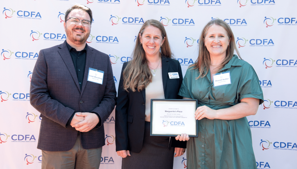 3 well-dressed adults stand holding a plaque in front of the NHCDFA backdrop at the awards ceremony